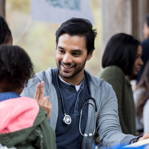 Volunteer doctor holds up two fingers as he checks a young girl's vision. The girl and her mom are visiting an outdoor free clinic.